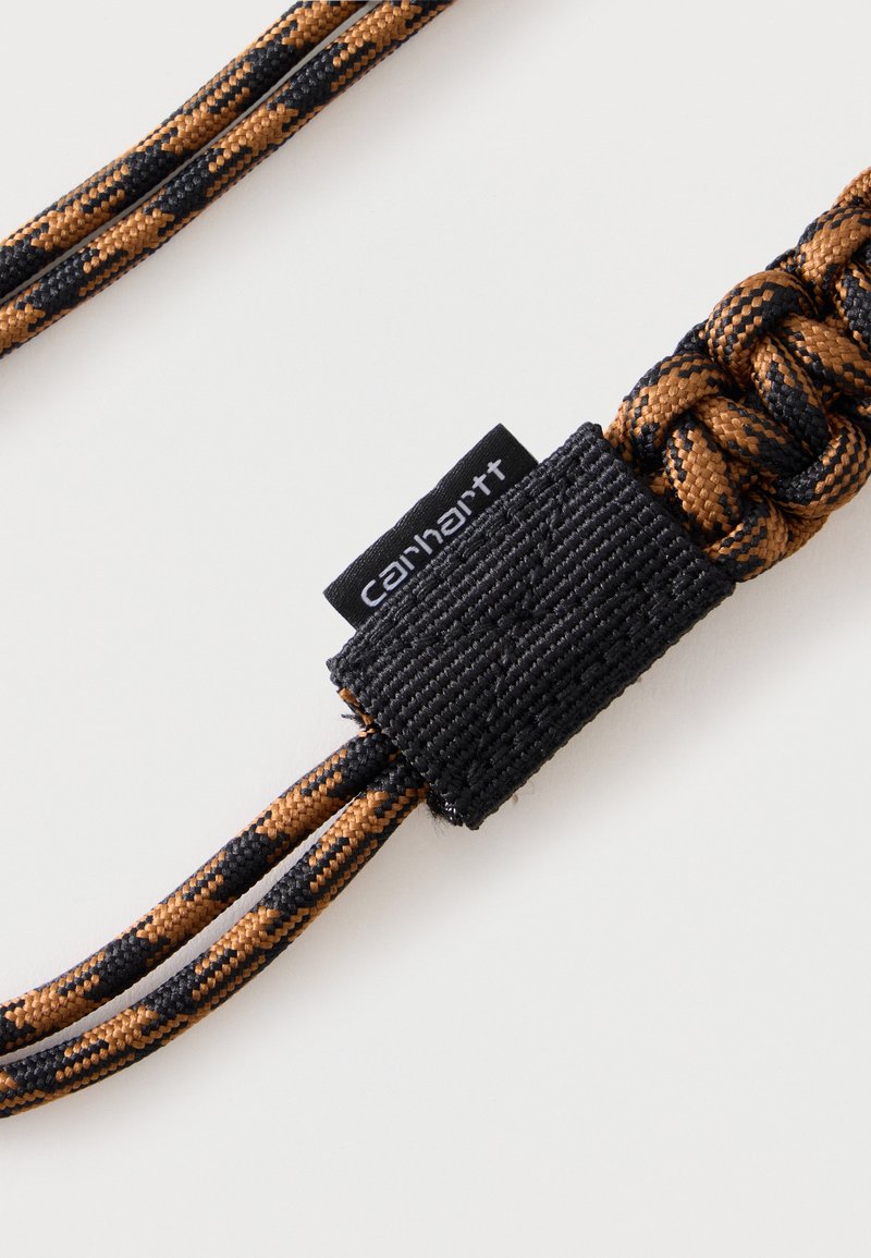 Brunt og sort flettet reb med et sort stofmærke med teksten "Carhartt" syet på mod en ensfarvet hvid baggrund.