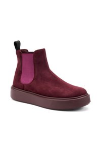 Botines de ante burdeos con paneles laterales elásticos en púrpura, que presentan una suela gruesa color marrón y una lengüeta negra en la parte posterior.