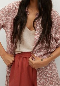 Chemise légère à motif floral en rose et blanc, portée sur un haut beige. Associée à un short couleur rouille à taille élastique.