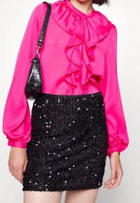 Blouse fuchsia vif avec col à volants et manches longues, assortie à une mini-jupe noire à sequins. L'ensemble comprend un petit sac noir.