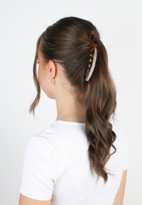 Clip per capelli in tartaruga con design curvo, caratterizzato da motivi crema e marrone scuro, tiene saldamente i capelli acconciati in una coda di cavallo.