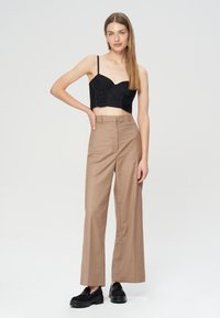 Czarny krótki top o strukturalnej talii, zestawiony z be�żowymi, szerokimi spodniami z wysokim stanem i czarnymi butami wsuwanymi.