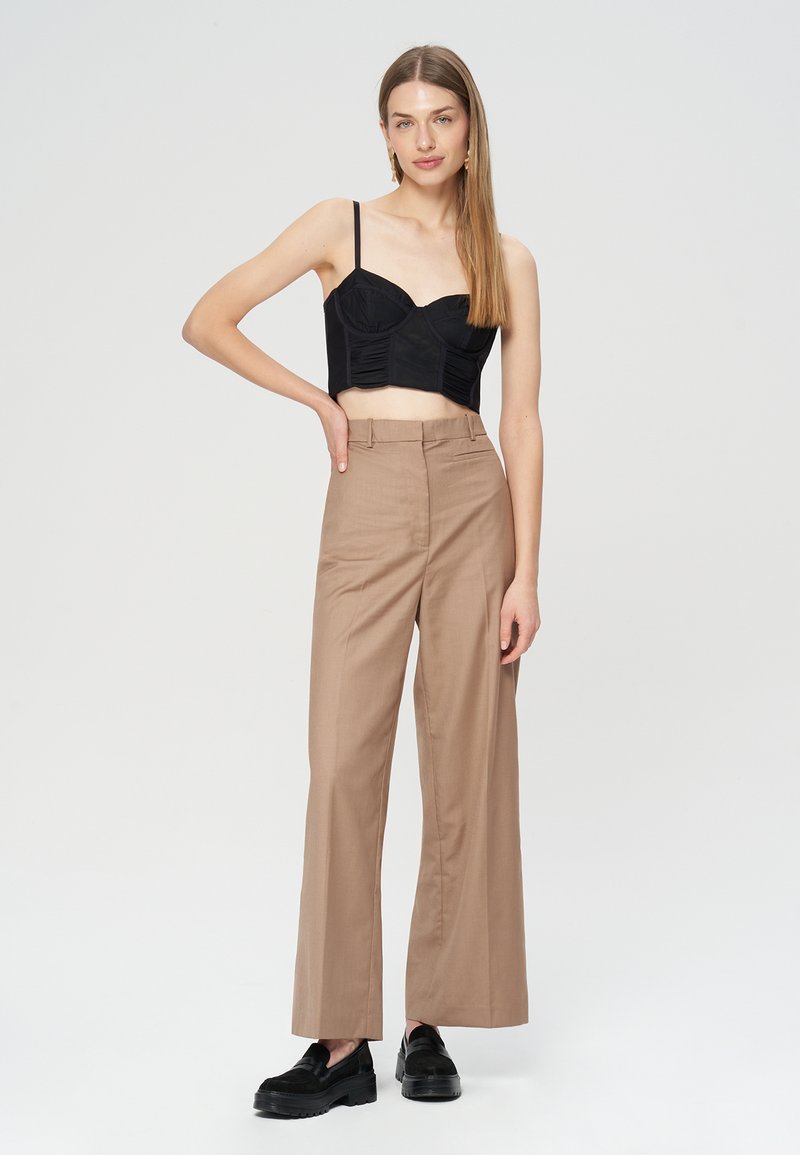 Czarny krótki top o strukturalnej talii, zestawiony z beżowymi, szerokimi spodniami z wysokim stanem i czarnymi butami wsuwanymi.