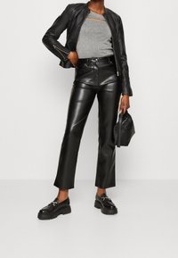 Giacca di pelle nera, top grigio aderente con aperture, pantaloni di pelle neri a vita alta e mocassini neri chunky con un accento argento.