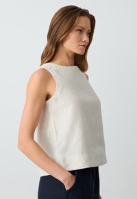 Jasno beżowy lniany top bez rękawów, z wysokim kołnierzem, prostym krojem i bocznymi rozcięciami. Gładka faktura i minimalistyczny design.
