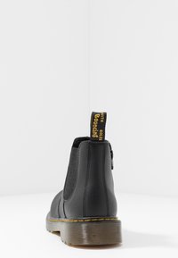 Svarta Chelsea-stövlar med elastiska sidopaneler, strukturerad gummisula och gul "Bond146" dragflik bak. Slät läderöverdel.