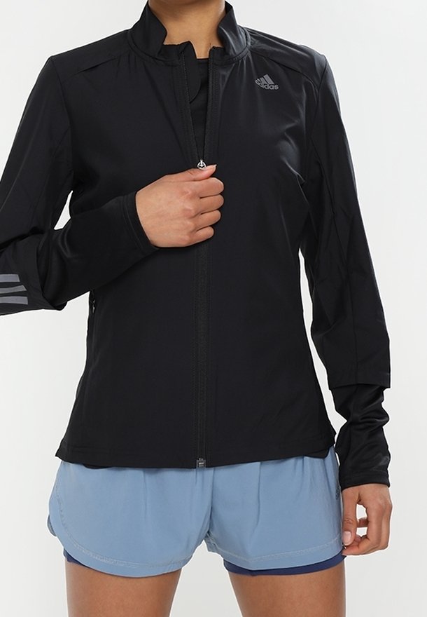 Veste de sport noire avec fermeture éclair à l'avant, col haut et manches longues. Montre un logo sur la poitrine et trois bandes sur la manche gauche.