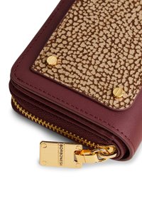 Nahaufnahme einer burgunderfarbenen Lederbörse mit strukturiertem beigen Deckel, der mit goldfarbenen Schrauben gesichert ist, und einem goldenen Reißverschlussanhänger, der mit "BORBONESE" graviert ist.