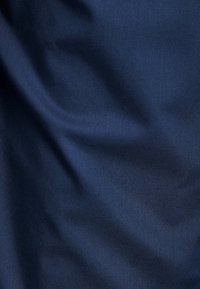 Granatowy, gładki materiał o subtelnym połysku i delikatnych fałdach, wskazujących na teksturę i wagę bez wyraźnych wzorów czy akcentów.