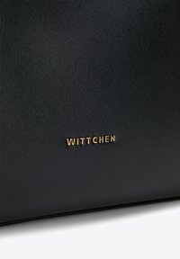 Sac à main en cuir noir avec une finition texturée, arborant un logo doré en relief "WITTCHEN" à l'avant. Design simple et élégant.