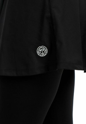 Zwarte rok met een klein wit rond logo met een gestileerd gezicht nabij de zoom, gedragen over zwarte legging.