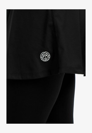 Zwarte rok met een klein wit rond logo met een gestileerd gezicht nabij de zoom, gedragen over zwarte legging.