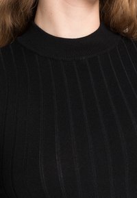 Black ribbed sweater featuring a high neck, smooth texture, and vertical stripes, highlighting a close-fitting design.