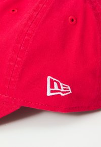 Cappello rosso con tessuto testurizzato, dotato di un logo bianco ricamato di lato. I punti di cucitura sono visibili, arricchendo i dettagli del design.