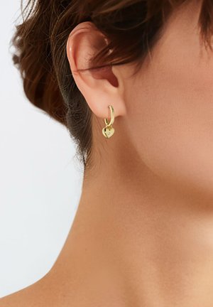 Boucle d'oreille en or avec un petit pendentif en forme de cœur et un accent de pierre précieuse claire. Le design met en valeur une finition polie et un look léger.