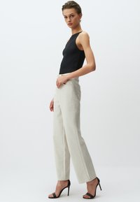 Zwarte geribde bodysuit met hoge halslijn. Lichtbeige wijde broek met zijzakken en zichtbare stiksels. Model in zwarte-hak sandalen.