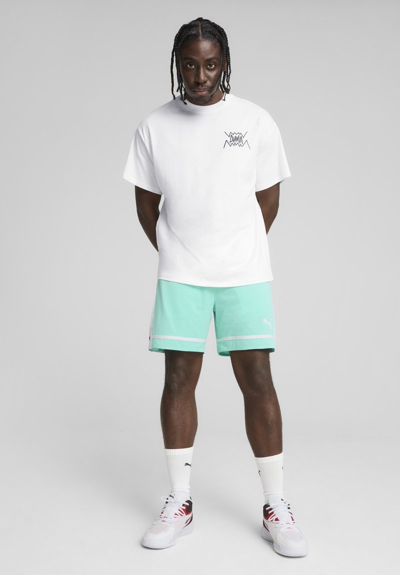 Hvid bomulds t-shirt med et sort grafisk design, parret med mintgrønne shorts med en hvid stribe. Båret med hvide sokker og multikolor sko.