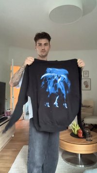 Sweatshirt preto com um design gráfico azul apresentando formas abstratas. Mangas longas, textura suave e decote redondo padrão.