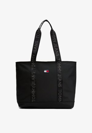 Czarna torba typu tote Tommy Jeans z szerokimi uchwytami, ozdobiona powtarzającym się napisem „Tommy Jeans” oraz małą czerwoną, białą i niebieską naszywką z logo na środku z przodu.