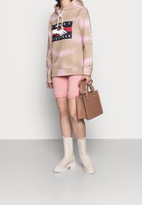 Felpa beige con logo e motivo tie-dye rosa, abbinata a pantaloni shorts rosa chiaro. Accompagnata da una piccola borsa marrone e stivaletti di gomma beige.