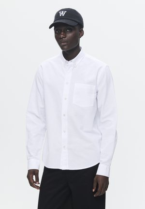 White button-up shirt with long sleeves, front pocket, and small logo embroidery. Paired with a black cap featuring a white logo.