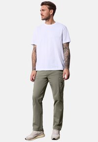 Camiseta de algodón blanca, ajuste casual. Pantalones cargo verde oliva con bolsillos laterales. Zapatillas ligeras beige. Diseño simple sin patrones visibles.