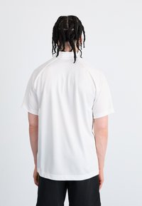 White short-sleeve athletic shirt with a round collar and raglan sleeves, featuring smooth, lightweight fabric and a relaxed fit.