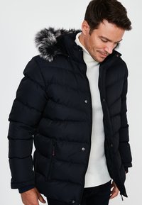 Marine pufferjack met een met bont afgewerkte capuchon, doorgestikte ontwerp en ritszakken. Heeft een hoge kraag en ribgebreide manchetten voor extra warmte.