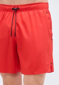 Κόκκινα μαγιό σορτς με ελαστική μέση, λεπτομέρεια με κορδόνι και πλαϊνές σχισμές. Κατασκευασμένα από ελαφρύ ύφασμα με ομαλή υφή.