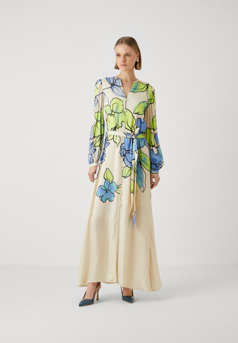 Lange, crème gekleurde bloemenjurk met blauwe en groene bladeren, lange pofmouwen, een tailleband en een V-halslijn. Gladde satijnen textuur.