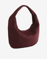 Sac à main hobo tissé rouge foncé, de forme arrondie, avec une bandoulière unique, posé sur un fond clair et uni.