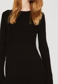 Abito a coste nero con maniche lunghe e scollatura rotonda. Il tessuto texturizzato crea una silhouette aderente.