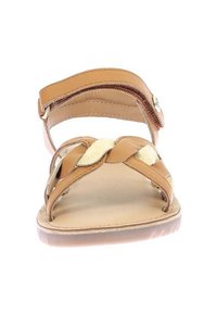 Sandalia de cuero marrón con tiras entrelazadas, correa trasera, plantilla natural lisa y una banda sutilmente texturizada a lo largo del pie. Suela transparente.