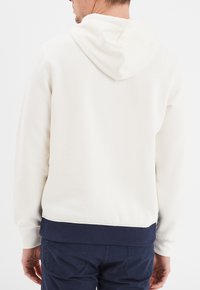Sudadera blanca con capucha ajustable, dobladillo inferior y puños de canalé en color marino, textura suave y diseño liso. Vista trasera sin detalles adicionales.