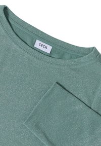 Lichtgroene longsleeve top met subtiele zilveren glans, ronde halslijn en zichtbaar "CECIL" merkje binnenin de kraag.