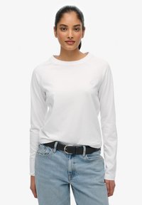 Witte langemouwenshirt met een ronde hals, gemaakt van zachte stof. Gecombineerd met lichtblauwe jeans en een zwarte riem.
