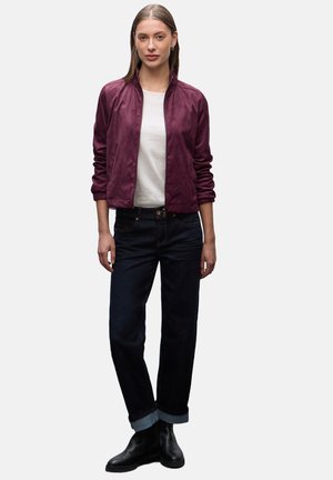 Veste bomber en satin bordeaux avec un col montant, associée à un jean noir avec un ourlet retroussé et des bottines noires. T-shirt blanc simple en dessous.