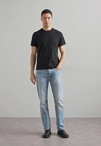 Svart bomulls t-skjorte kombinert med lyseblå denimjeans. Modellen har på seg svarte ankelstøvler og står på en nøytral grå bakgrunn.