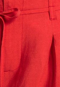 Roter Leinenstoff mit gebundenem Taillenbund, subtiler Textur und einer Seitentasche, sauber genähten Nähten und einem leichten Faltendetail.