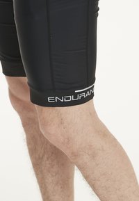 Pantalones cortos deportivos negros elaborados con material elástico, que cuentan con costuras en contraste, un diseño ajustado y un destacado logo "ENDURAN" en el dobladillo.