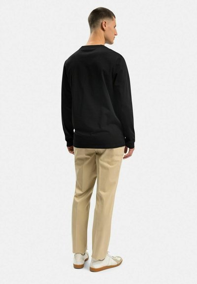 Svart langärmad skjorta, avslappnad passform, kombinerad med beige byxor. Skorna är vita med ljusbruna sulor. Enkel och funktionell design.