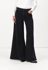 Zwarte wijduitlopende jeans van denim met een hoge taille, voorzien van zijzakken en een relaxte pasvorm, weergegeven met een witte top.