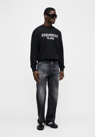 Schwarzer Sweatshirt mit dem Logo "DSQUARED2 MILANO", abgenutzte graue Jeans und schwarze Turnschuhe mit weißen Streifen. Accessoires sind dunkle Sonnenbrillen.