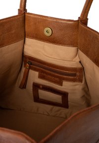 Binnenkant van een tan leren handtas met een beige stoffen voering, een ritsvak en een magnetische drukknoopsluiting.