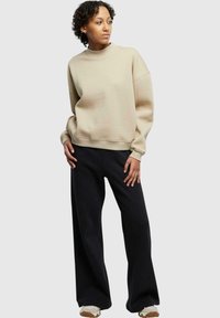 Lys beige kort genser med høy hals, senkede skuldre og ribbestrikkede ermer, kombinert med svarte vide bukser og joggesko.