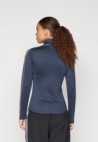 Námořnická modrá dlouhá rukávová halenka s vysokým límcem, se bílými bočními pruhy, přiléhavým střihem a texturovanou tkaninou. Vhodná pro aktivní nošení.