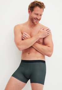 Gestreepte boxershorts in donkergroen met een marineblauwe tailleband. Zacht, rekbaar materiaal dat zich aan het lichaam vormt voor comfort. Middelste dijlengte.