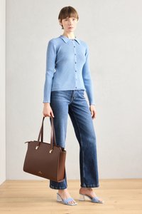 Bolso tote de cuero marrón con herrajes dorados, cárdigan de punto azul, jeans acampanados de mezclilla azul y sandalias de tacón azul claro sobre un suelo de madera.