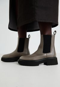 Botines de cuero gris con paneles elásticos en los lados, suela negra gruesa y lengüeta trasera para facilitar el calzado. Acabado texturizado en el cuero.