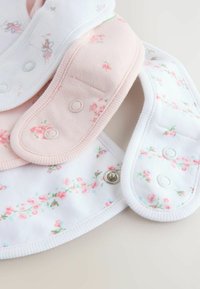 Három virágmintás babakötény patentos rögzítéssel, fehér és pasztell rózsaszín színekben, átlapolva elrendezve egy világos felületen.